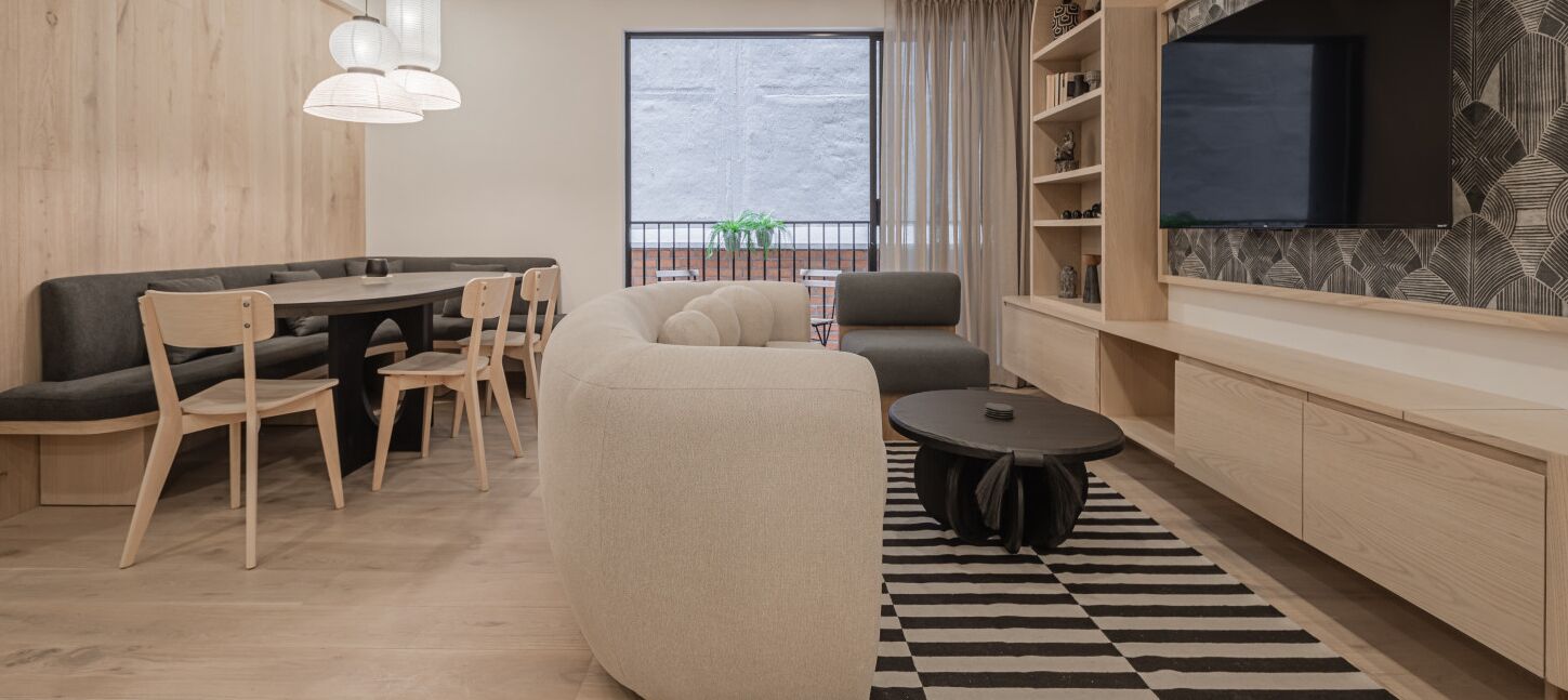 Ein modernes Wohnzimmer mit einer Couch, Sesseln, einem Esstisch, einem Fernseher und einem Bücherregal.