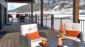 A covered outdoor seating area with wicker furniture and orange cushions, overlooking a snowy landscape with mountains. - Riverside Luxury: Private River Float with Hot Tub and 3 King Suites! (Lava Hot Springs)