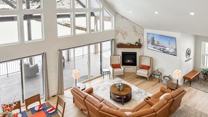 A spacious living room with a fireplace, large windows, and a high ceiling. - Riverside Luxury: Private River Float with Hot Tub and 3 King Suites! (Lava Hot Springs)