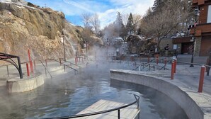 A hot spring area with a wooden platform and metal railings. - Riverside Luxury: Private River Float with Hot Tub and 3 King Suites! (Lava Hot Springs)
