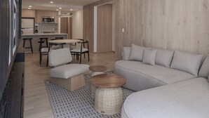 A modern living room with a sofa, ottoman, and coffee table, a dining area with chairs, and a kitchen in the background. - Luxurious Apartment In La Condesa (Ciudad de México)