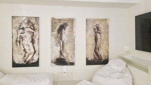 Een kamer met drie grote abstracte schilderijen aan de muur, een bed met witte beddengoed en een nachtkastje met een lamp.