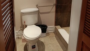 Une petite salle de bain comprenant des toilettes, une douche et une fenêtre avec des stores.