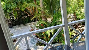 Un espace extérieur aménagé avec des sièges, abrité et doté de chaises en métal et d’une table, le tout entouré d’une végétation luxuriante et de diverses plantes.