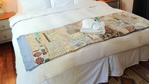 Un lit bien fait, recouvert d’une courtepointe, avec un tableau au-dessus et deux lampes de chevet.