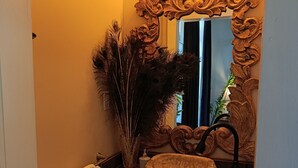 Une salle de bain avec un meuble-lavabo, un miroir orné de motifs sculptés et une décoration en plumes de paon.