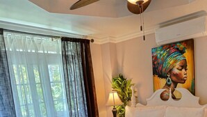 Une chambre d’hôtel avec un grand lit, un ventilateur de plafond, un tableau au mur et une fenêtre avec des rideaux.