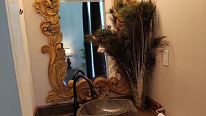 Une salle de bain avec un lavabo en pierre, un miroir doré orné et des plumes de paon.