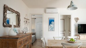 A spacious living area with a wooden dining table, white chairs, a large mirror, and a television.