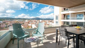 Uma varanda com mesa e cadeiras, com vista para uma paisagem urbana e montanhas ao longe.