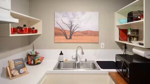 A kitchen with a double sink, a microwave, and a painting of a tree on the wall. - Midtown Gem! Sleeps 3 Near Richmond and Montrose (Houston)