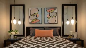 A bedroom with a patterned bedspread, two wall-mounted abstract paintings, and bedside lamps. - Midtown Gem! Sleeps 3 Near Richmond and Montrose (Houston)