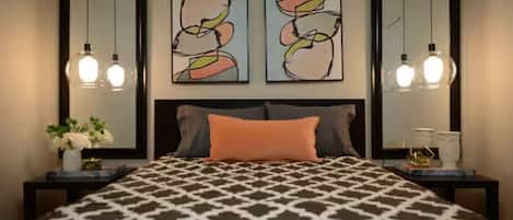 A bedroom with a patterned bedspread, two wall-mounted abstract paintings, and bedside lamps.