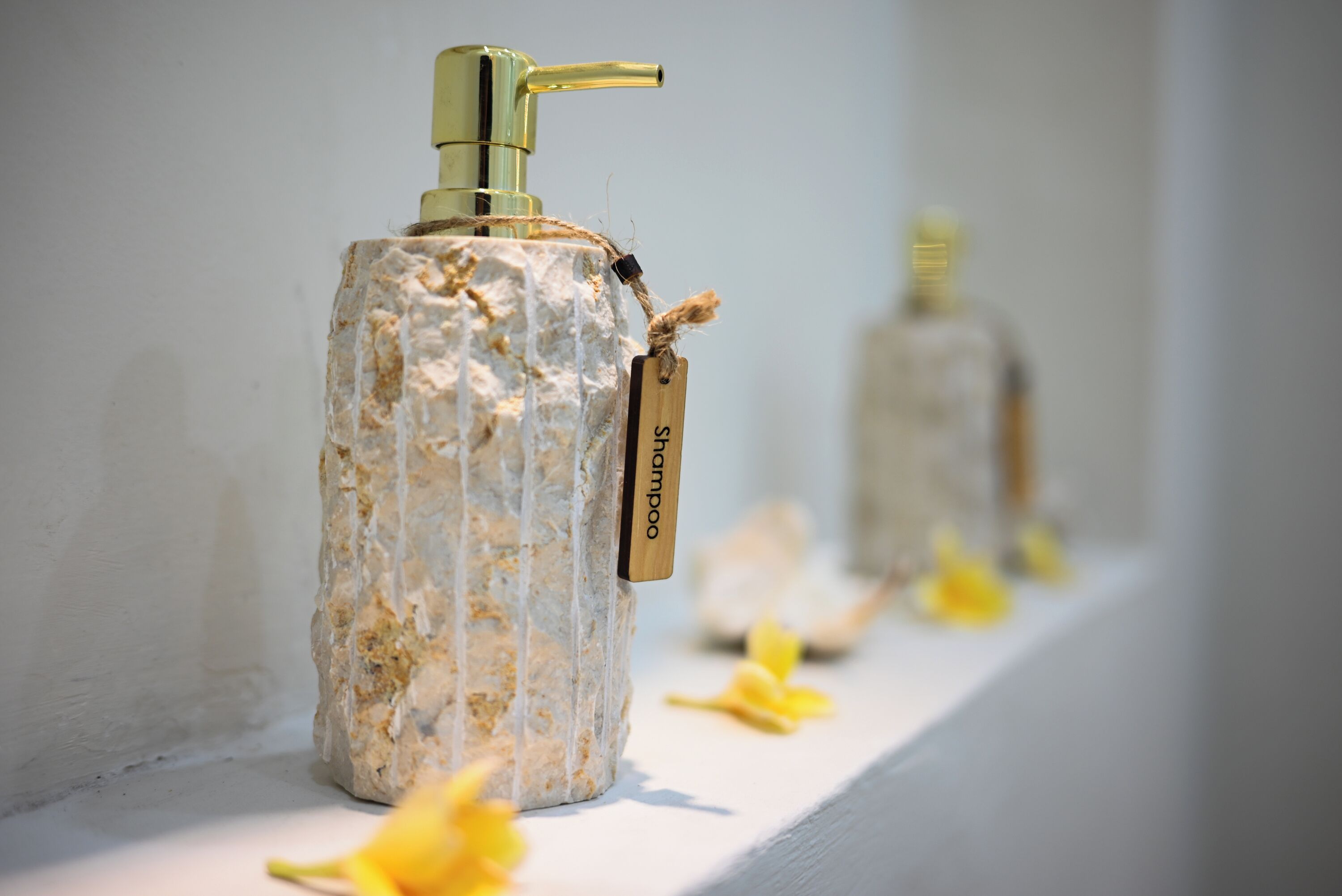 A bathroom with a white sink, a gold faucet, and a bottle of shampoo.