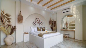 Une chambre moderne avec un grand lit, des œuvres d’art décoratives au mur, un luminaire suspendu et un petit tabouret.