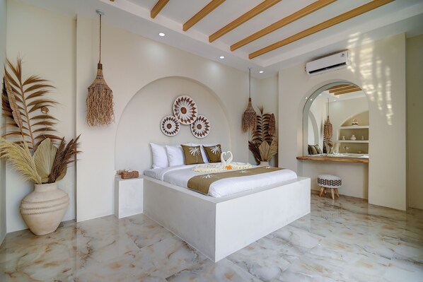 A modern bedroom with a large bed, decorative wall art, a hanging light fixture, and a small stool. - The Medusa Villas Bali (Kuta)