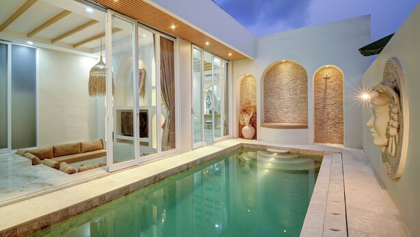 Un espace piscine intérieur moderne, doté de murs en verre, d’un plafond en bois et d’éléments décoratifs en pierre.