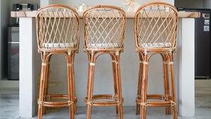 Une cuisine avec trois chaises en osier, un îlot central blanc et deux suspensions en osier.