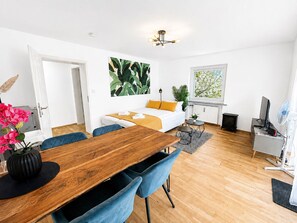 Ett modernt vardagsrum med ett matbord i trä, blå stolar, en soffa med gula kuddar, en öppen spis och ett stort fönster med utsikt över grönområden.