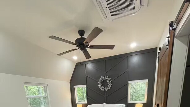 Un dormitorio con una cama, dos mesitas de noche, un ventilador de techo y un aire acondicionado de pared.