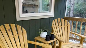 Dos sillas Adirondack sobre una terraza de madera con una pequeña mesa y una planta en maceta.