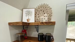 Una cocina con estantes de madera, microondas, cafetera y una cesta de aperitivos.