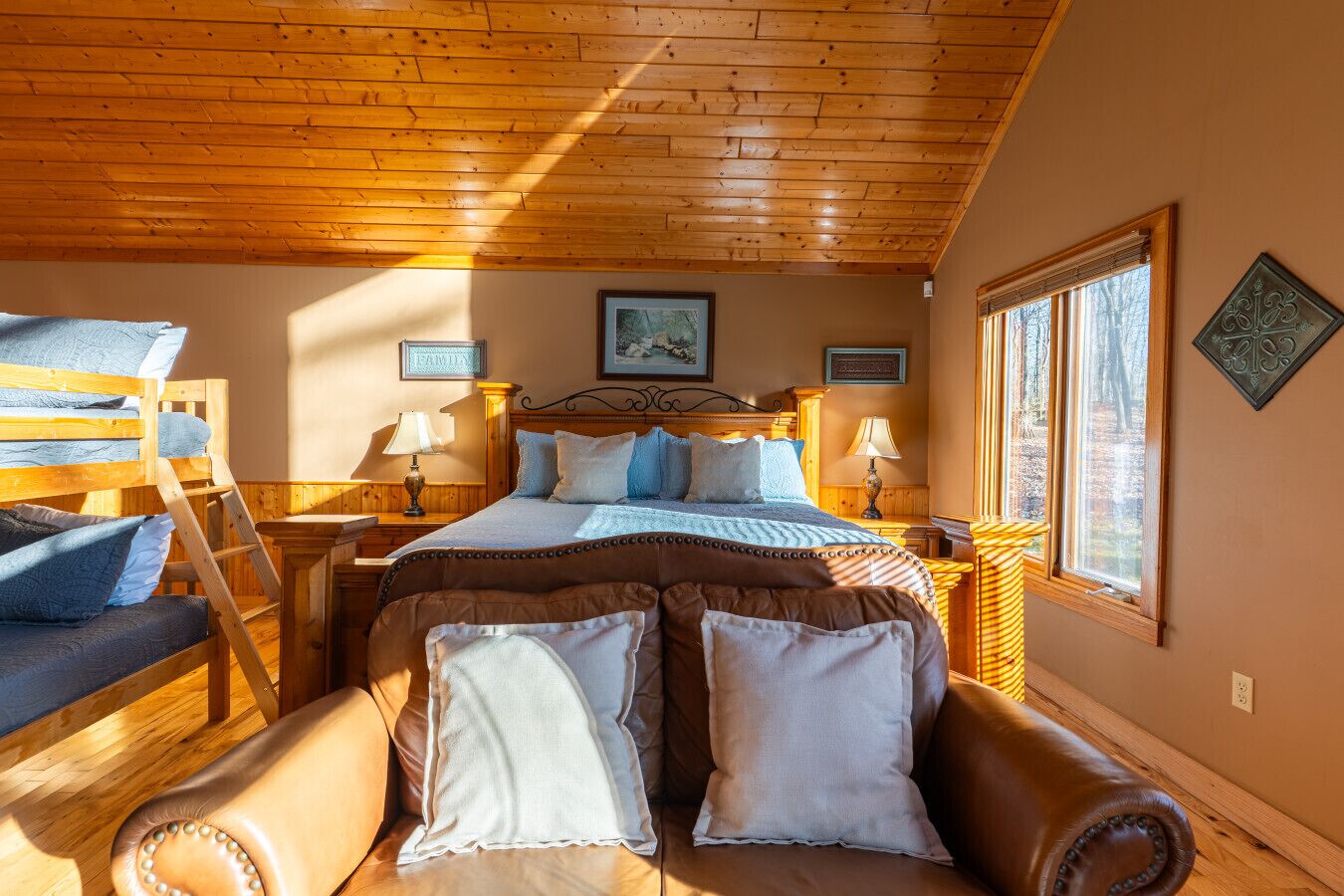 Une chambre confortable avec un plafond en bois, un grand lit doté de plusieurs oreillers, une chaise en bois et une fenêtre avec des stores.
