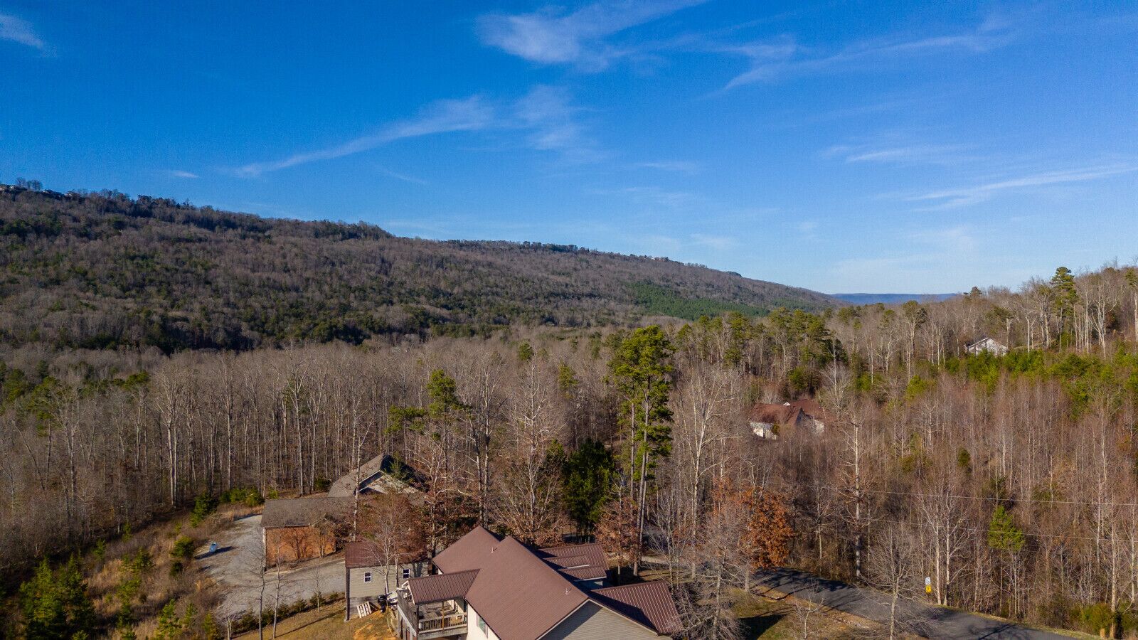 A residential area with houses surrounded by dense forest and hills in the background.