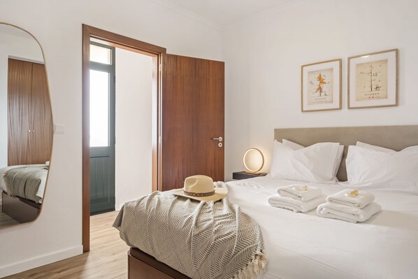 Habitación de hotel con cama, mesita de noche con lámpara, espejo, puerta y pared con cuadros.