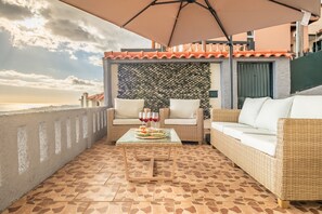 A balcony with wicker furniture, a table with drinks, and a view of the sea.