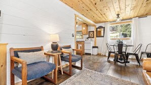 Une pièce chaleureuse avec un plancher en bois, un coin repas comprenant une table et des chaises, un canapé et une petite cuisine.