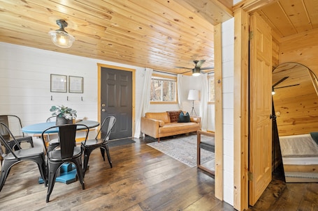 A wooden interior with a dining area, a sofa, and a ceiling fan.