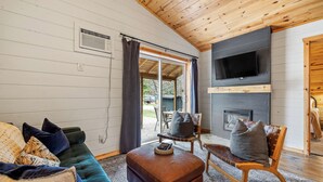 A cozy living room with a green sofa, a brown ottoman, a wooden chair, and a flat-screen TV mounted above a fireplace. - The Minnesota Ridge Cabin (Keystone)