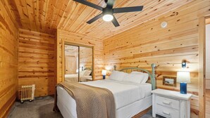 A wooden-paneled bedroom with a bed, nightstand, and ceiling fan. - The Minnesota Ridge Cabin (Keystone)