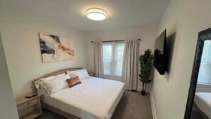 A bedroom with a bed, a nightstand, a potted plant, a window with curtains, and a ceiling light.