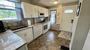 A kitchen with white cabinets, a granite countertop, a stove, a microwave, and a window with curtains.