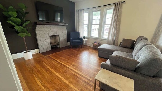 A living room with a fireplace, a grey sofa, a small table, and a potted plant.