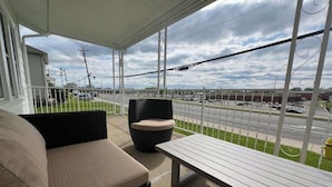 A covered outdoor seating area with a bench and two chairs, overlooking a parking lot and a road.