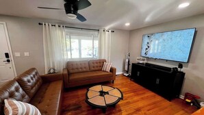 Ein Wohnzimmer mit braunem Ledersofa, einem runden Couchtisch, einem Deckenventilator, einem Flachbildfernseher und einer schwarzen Unterhaltungsecke.