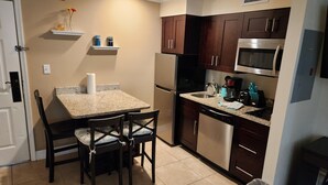 A compact kitchen with dark wooden cabinets, a stainless steel refrigerator, a microwave, and a dishwasher. There is a small countertop with a sink and a coffee maker. - Comfortable Family Disney Orlando Universal (Kissimmee)