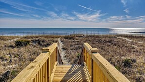 A wooden boardwalk leading to a beach with a clear sky.