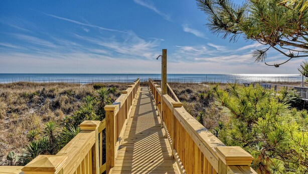A wooden boardwalk leading to a beach with a clear sky.