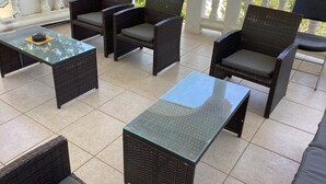 An outdoor patio area with wicker furniture, including chairs and tables, and a tiled floor. - Colwins #2 For Families/Couples/Singles Sleeps 4 (Cockburn Town)