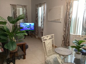 Una sala de estar con televisión, una mesa de vidrio, sillas y una planta grande.
