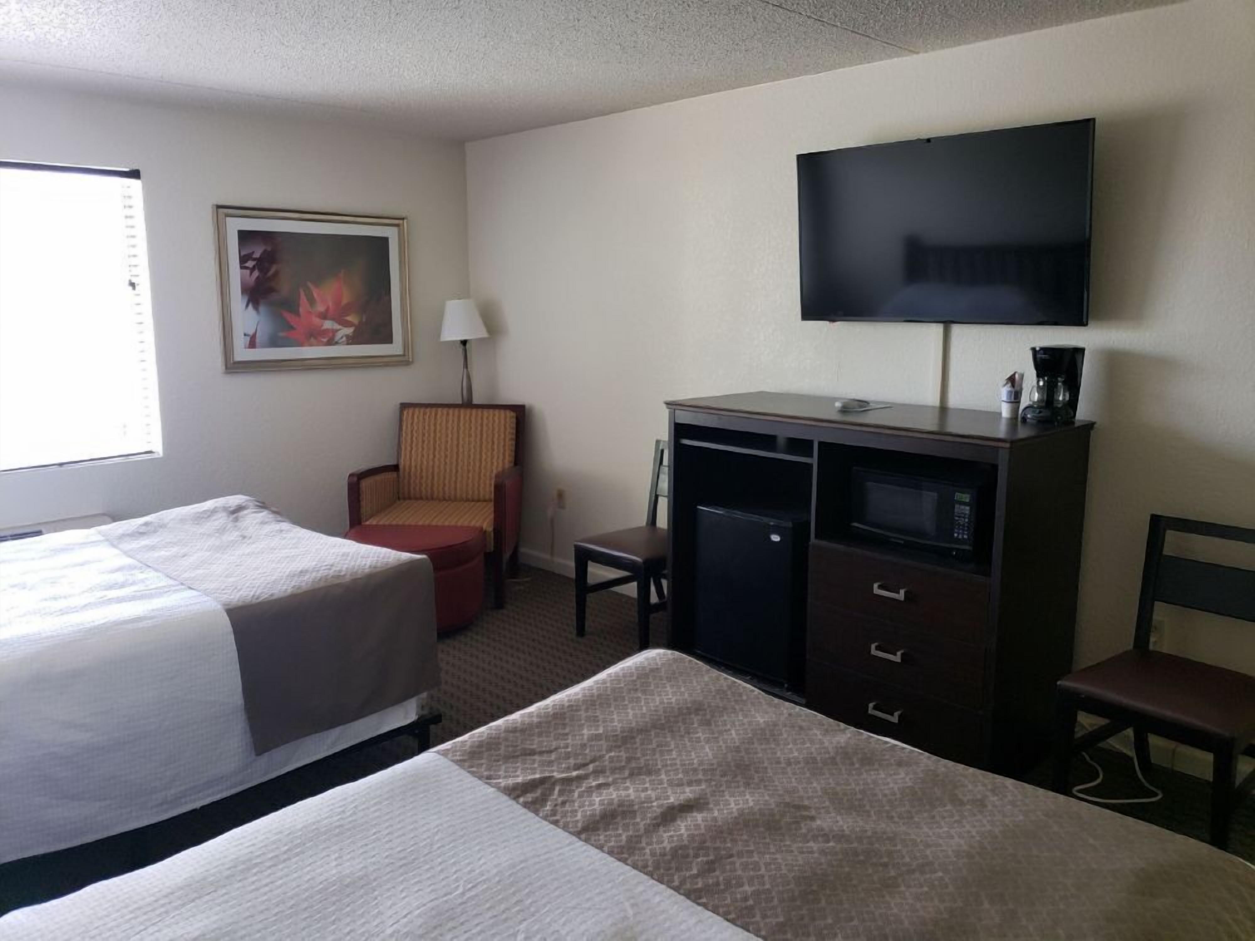 A hotel room with two beds, a desk with a microwave, a television, and a chair.
