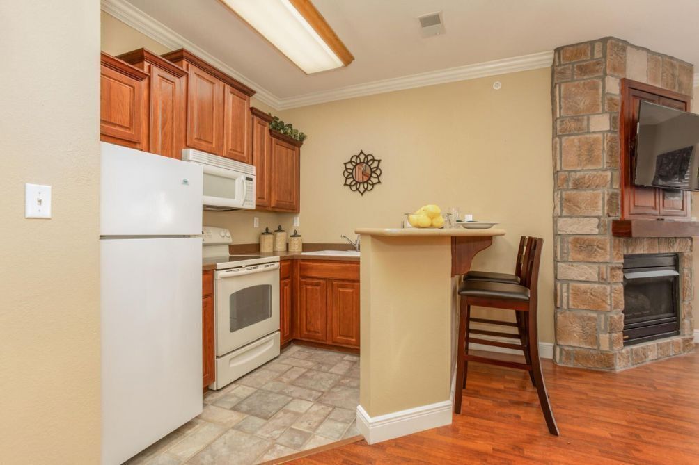 A kitchen with wooden cabinets, a white refrigerator, a stove, a sink, and a stone fireplace.