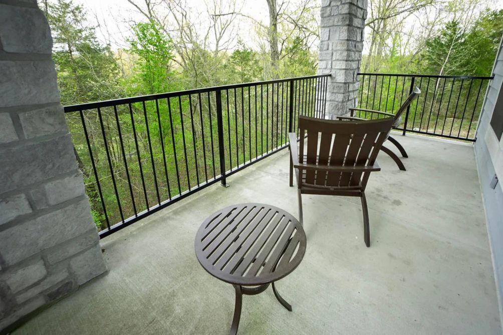 Ein Balkon mit rundem Tisch, zwei Stühlen, einer Steinsäule und einem schwarzen Metallgeländer.
