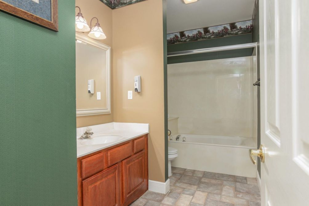 A bathroom with a wooden vanity, a large mirror, a shower with a glass door, and a tiled floor.