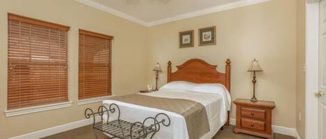 A bedroom with a bed, two bedside tables, a ceiling fan, and two windows with blinds.