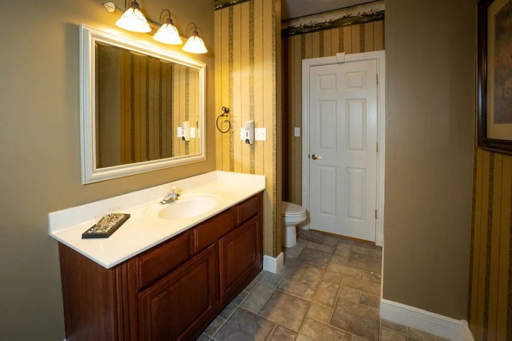 A bathroom with a large mirror, a double sink vanity, a toilet, and a door.
